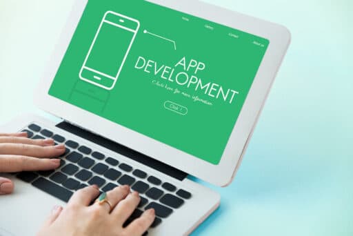 Mains tapant sur un ordinateur portable affichant une page de destination verte avec le texte "App Development" et une icône de téléphone minimaliste.