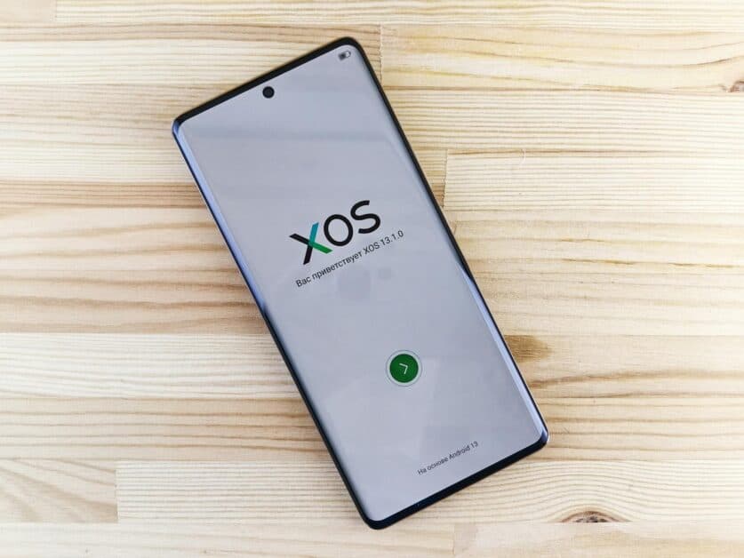 Écran d'accueil d'un smartphone Android affichant le logo XOS 13 sur un fond de bois clair, symbole d'une interface utilisateur personnalisée.