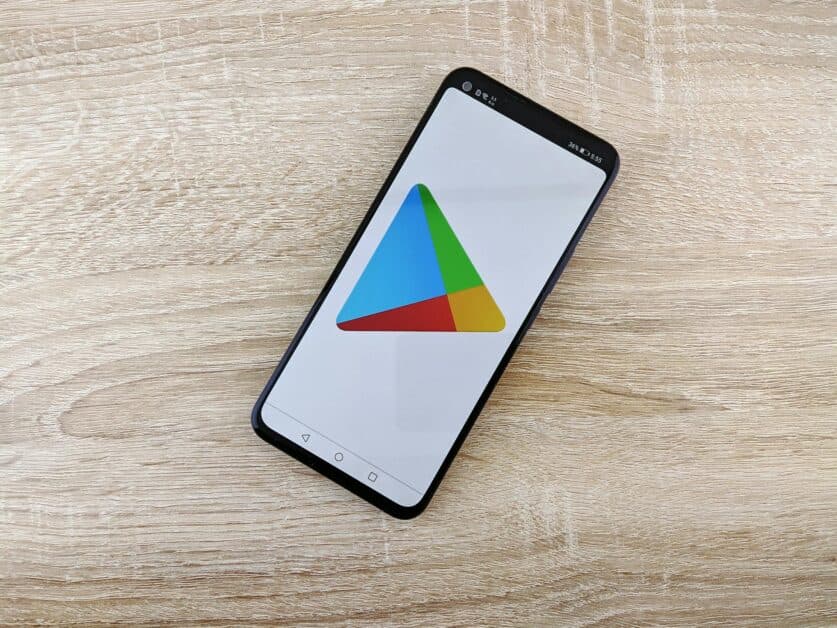 Smartphone posé sur un bureau en bois affichant le logo coloré du Google Play Store, la plateforme finale de déploiement pour toute création d'application mobile.