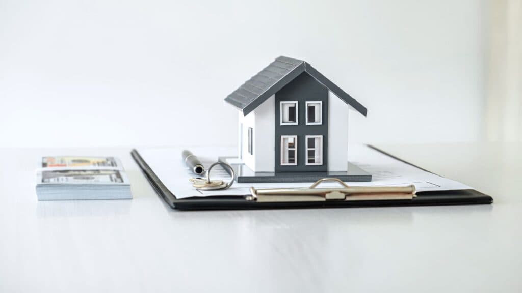 Maquette de maison posée sur un porte-bloc avec des clés et des liasses de billets illustrant le financement sur une application immobilier